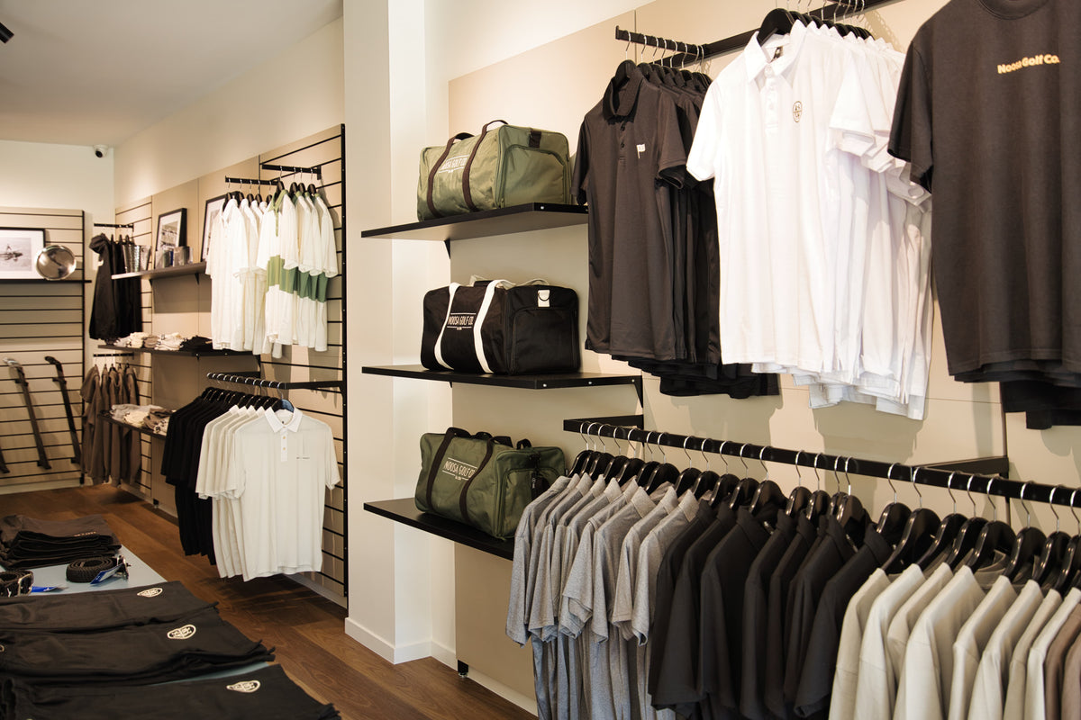 Apparel display inside Noosa Golf Co., a premium Sunshine Coast golf shop. Golf polos, tees, shorts, belts, and duffle bags neatly arranged in-store, showcasing quality gear and clean design.
