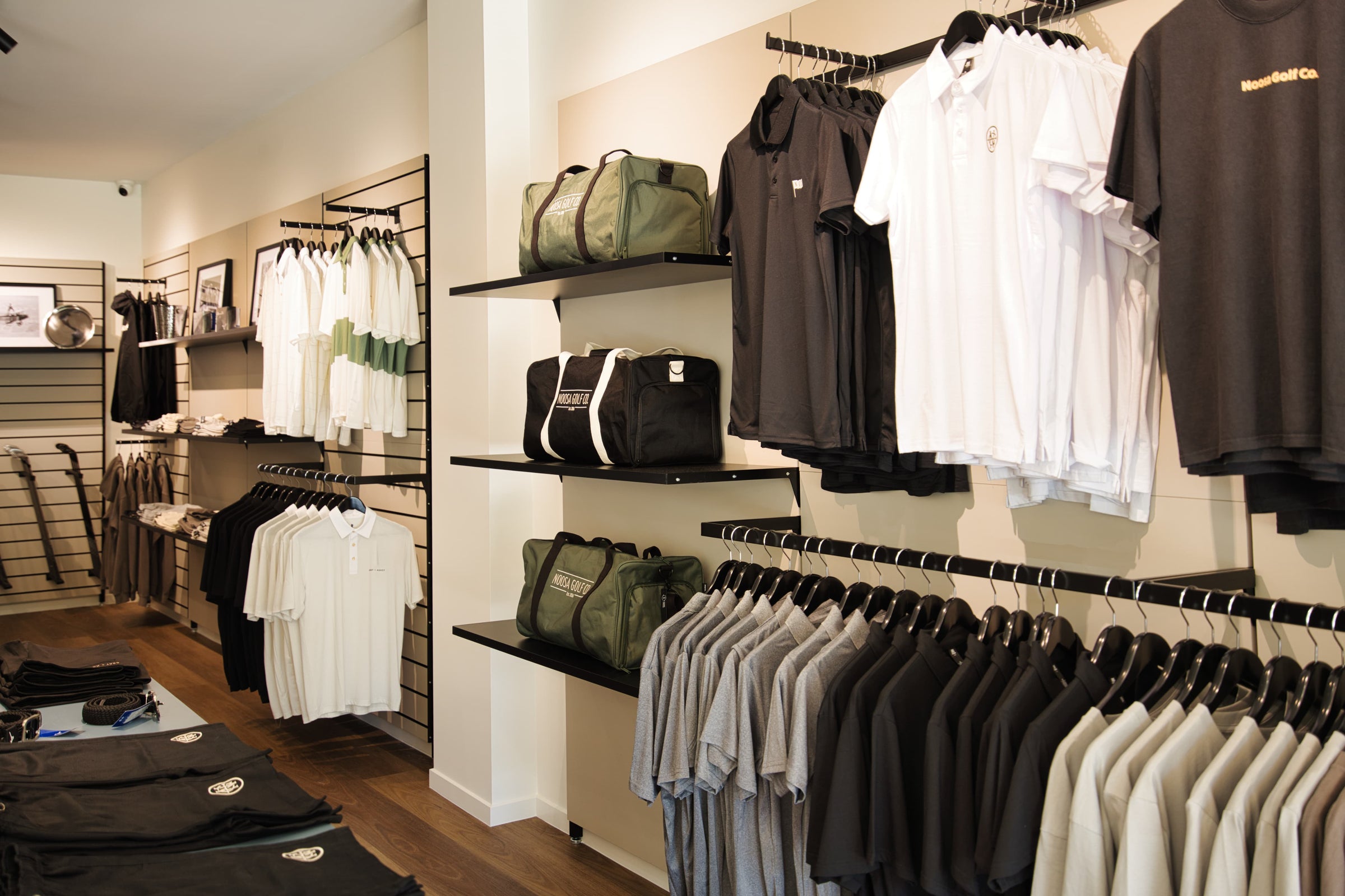 Apparel display inside Noosa Golf Co., a premium Sunshine Coast golf shop. Golf polos, tees, shorts, belts, and duffle bags neatly arranged in-store, showcasing quality gear and clean design.